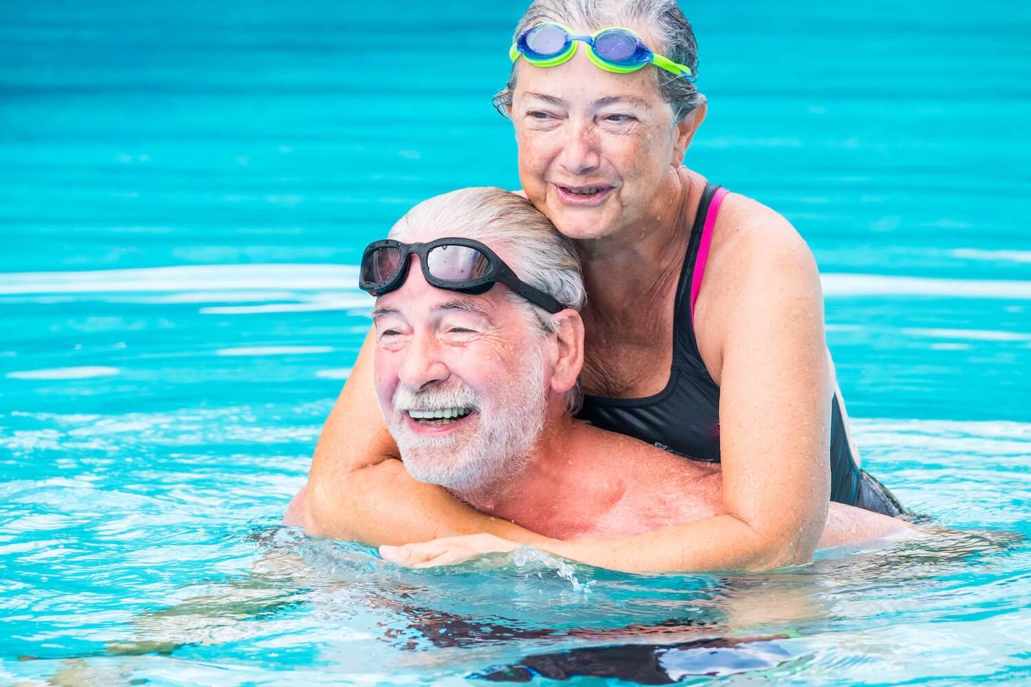 two pensioners or mature old people enjoying summer and vacations in the swimming pool together having fun smiling and laughing - couple of cute seniors in love - happy lifestyle and healthy concept